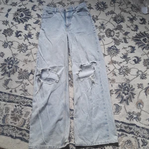 Ljusblåa wide jeans med slitna knän - Ljusblå jeans med breda ben och rejält slitna hål över båda knäna. Klassisk femficksmodell i denim med hög midja och raka, vida ben. Perfekt för dig som gillar en avslappnad och edgy stil och är från H&M säljer dessa eftersom de blivit försmå på mig ⭐️