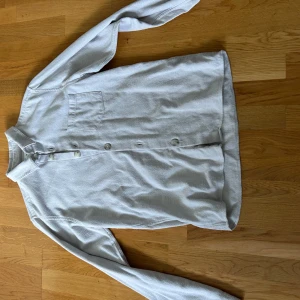 Ljusgrå skjorta från Ciszere, slim fit - Snygg ljusgrå skjorta från Ciszere i slim fit-modell. Skjortan har klassisk krage, knäppning framtill och en bröstficka. Tillverkad i mjukt bomullstyg som känns skönt mot huden. Perfekt för dig som gillar stilrena och enkla plagg.