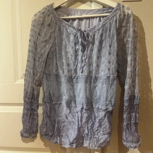 Ljuslila blus med spets och paljetter M&G - Superfin ljuslila blus från M&G med transparenta spetsärmar, broderade detaljer och paljetter vid halsringningen. Blusen har knyt framtill och är i ett tunt, luftigt material som känns riktigt drömmigt. Perfekt för dig som gillar romantisk och bohemisk stil.