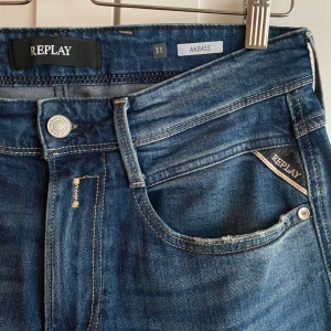 Replay Anbass jeans blå herr - Snygga Replay Anbass jeans i klassisk blå tvätt med lätt slitning och raka ben. Jeansen har fem fickor, Replay-logga på myntfickan och bakficka samt läderpatch bak. Perfekt passform och stilren look för dig som gillar denim.