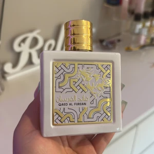 Qaed Al Fursan Eau de Parfum - Snygg parfymflaska i vit keramik med guldig dekor och ett stilrent mönster på framsidan. Flaskan har en lyxig, rundad guldig kork och detaljer med hästmotiv. Eau de Parfum tillverkad i Förenade Arabemiraten, 80 ml.