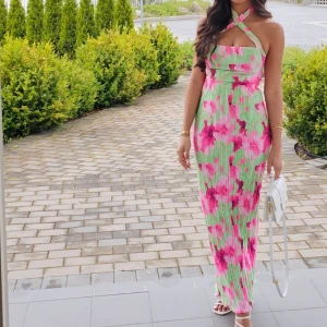 Grön långklänning med rosa blommor - Säljer en superfin set med grönt och rosa blommigt mönster. Materialet är lätt och plisserat, perfekt för varma dagar. Passformen är slim och klänningen har en feminin siluett.