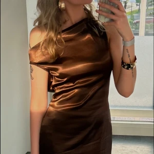 Brun lång satinklänning med öppen rygg - Säljer min balklänning! Bara använd en gång och i jättebra skick. Slutar precis över anklarna för mig som är 170 cm