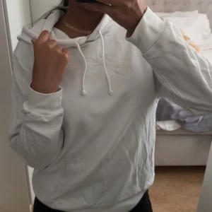 Vit hoodie med snörning - Säljer en stilren vit hoodie med snörning i halsen och huva. Tröjan har långa ärmar och ribbade muddar vid ärmslut och nederkant. Perfekt för chill dagar och enkel att matcha med jeans eller mjukisbyxor.