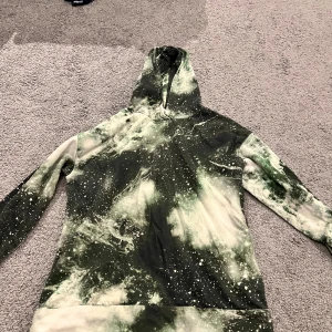 Grön och vit hoodie från Lindex - Säljer en hoodie från Lindex i storlek 170 med coolt grönvitt mönster som påminner om rymden eller batik. Tröjan har huva och långa ärmar, perfekt för dig som gillar unika plagg med streetkänsla.