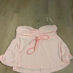 Ljusrosa broderad tubtopp med knyt - Supersöt ljusrosa tubtopp med broderade detaljer och ett fint knyt framtill. Toppen har bandeau-modell och är ärmlös, perfekt för varma dagar. 
