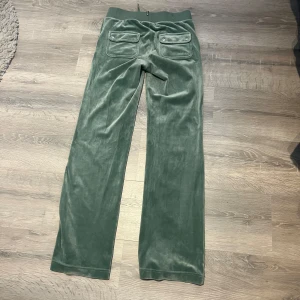 Juicy couture byxor - Mysiga gröna mjukisbyxor i mjuk velour med bred resår och snörning i midjan. Byxorna har raka ben, stora fickor fram och bak med knappdetaljer. Perfekta för chill dagar eller när du vill vara extra bekväm.