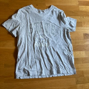 Grå t-shirt med STATE-print från H&M - Snygg grå t-shirt från H&M i storlek XS med coolt vitt STATE Football-tryck på framsidan. 
