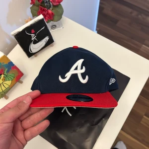 Atlanta Braves keps New Era 9FIFTY - Snygg Atlanta Braves snapback keps från New Era 9FIFTY-serien. Mörkblå krona med röd skärm och vit broderad A-logga framtill. Justerbar baktill med snapback. MLB-logga broderad bak. Perfekt för dig som gillar sportig streetstyle.