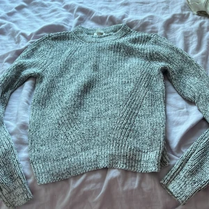 Grå stickad tröja från BASICS - Säljer en snygg gråmelerad stickad tröja från BASICS i storlek S. Tröjan har långärmade raglanärmar, rund hals och ribbade muddar. Materialet är mjukt och grovstickat, perfekt för kyliga dagar. Passformen är normal och färgen är en mix av ljusgrå och mörkgrå toner.