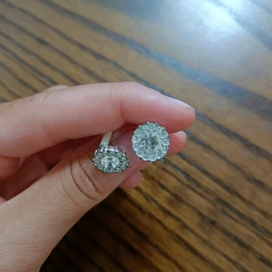 Glittriga silverörhängen med stenar - Säljer ett par runda örhängen i silverfärg med gnistrande stenar i mitten och runt kanten. Perfekt för dig som gillar bling och vill ha något som syns! Stenarna ger en riktigt glittrig effekt och örhängena är lätta att matcha med olika outfits.