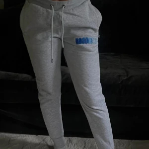 Grå mjukisbyxor från Hoodrich XS - Grå mjukisbyxor från Hoodrich i storlek XS. Byxorna har dragsko i midjan, broderad blå logga på benet och ribbade muddar vid bensluten. 