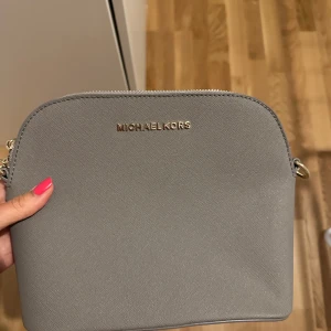 Grå axelväska  - Snygg grå axelväska med guldfärgade detaljer och kedja på axelremmen. Köpt utomlands