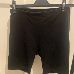 Svarta cykelshorts från H&M Basics - Svarta, enkla cykelshorts från H&M Basics i stretchigt material. De har en midwaist passform och är perfekta för en sportig look eller till vardagsoutfiten. Mjuka och bekväma med en tight passning som sitter snyggt på kroppen.