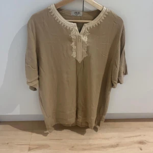 Beige marockans t shirt  - Säljer en beige henley med snygga broderade detaljer runt halsen och vid öppningen framtill. Skjortan har korta ärmar och är tillverkad i ett mjukt material som känns skönt mot huden. Perfekt för dig som gillar stilrena plagg med unika detaljer.