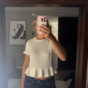 Vit stickad topp med volang från H&M - Supersöt vit stickad topp från H&M med korta ärmar och volangdetaljer vid ärmslut och nederkant. Mönstrad struktur i tyget och rund halsringning.💗