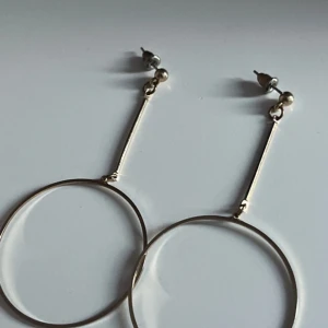 Stora cirkelformade örhängen i silver - Säljer ett par stora, minimalistiska örhängen i silverfärgad metall. De har en tunn, rund cirkelformad design som hänger i en smal stav från örsnibben. Perfekta för dig som gillar stilrena och trendiga accessoarer.