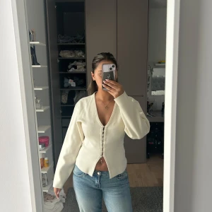 Krämvit kofta från Gina Tricot - Säljer en krämvit, kofta från Gina Tricot med v-ringning och snygga knappar framtill. Koftan är stickad och har långa ärmar. Enkel och clean design som funkar till jeans eller kjol.🩷helt slutsåld, aldrig använd. 