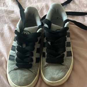 Adidas Campus grå sneakers mocka -  säljer super snygga Gråa Adidas Campus sneakers i mocka med svarta läderdetaljer och klassiska tre ränder på sidorna. Skorna har svart snörning, vit mellansula och gummisula. Adidas logga på hälen och Campus-tryck på sidan. Perfekt för en clean och stilren look. kan tänka mig gå ner  i pris. säljs då de tyvärr ej kommer till användning mer. köp ej direkt, skriv innan köp  ligger uppe på annan sida oxå🙂