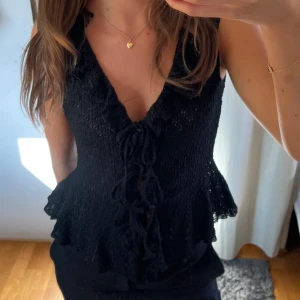 Svart linnetopp med snörning - Supersnygg svart linnetopp med djup v-ringning och volangkant. Aldrig använd, lappen sitter kvar!