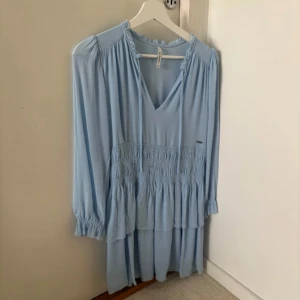 Ljusblå volangklänning  - ljusblå klänning med v-ringning, långa ärmar och volangdetaljer. 