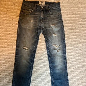 Tiger Of Sweden jeans med slitningar  - Säljer ett par blå Tiger Of Sweden jeans med snygga slitningar och hål på framsidan i storlek 30/32. Jeansen har klassisk femficksdesign, normal/slim passform. De har några defekter, lagning i skrevet och några trådar har lossnat som gör bakkappan lite lös, därav priset. 