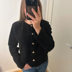 Svart kofta med guldknappar - Säljer en svart teddykofta/ jacka med rund halsringning och snygga guldknappar framtill. Jackan är croppad och har lång ärm. Använd 1 gång🩷