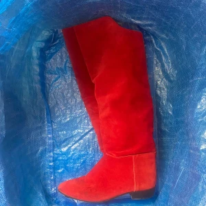 Röda mockastövlar med spetsig tå - Snygga knähöga stövlar i röd mocka med spetsig tå och låg klack. Perfekta för dig som vill sticka ut med färg och stil. De har en klassisk form och är tillverkade i mjukt mockamaterial. Lite små i storleken, passar 39/40.