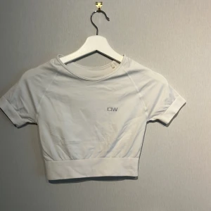 Vit träningstopp  - Vit croppadtränings topp från ICANIWILL med korta ärmar och rund hals. Toppen har en bred ribbad kant nedtill och diskret logga framtill.  Mjukt och stretchigt material!