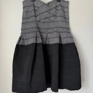 Svart och grå kortklänning med struktur - Säljer en snygg kortklänning i svart och grått med strukturerat tyg och vågigt mönster upptill. Kjolen är voluminös och har en markerad midja. Perfekt för dig som gillar en cool och modern look med lite edge.
