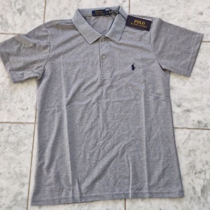 Grå piké från Polo Ralph Lauren - Snygg grå pikétröja från Polo Ralph Lauren med klassisk krage och två knappar framtill. Diskret broderad logga i mörkblått på bröstet. T-shirten är kortärmad och har en stilren, normal passform. Perfekt för en chill och clean look. Storlek S passar XS. Kom DM vid minsta fråga! 🍾 Mvh Savix_Resell