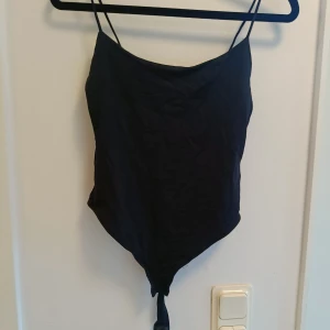 Svart linnetopp med knyt - Snygg svart linnetopp med smala axelband och knyt längst ner. Toppen har en spetsig nederkant och är perfekt för att skapa en trendig look. Enkel och stilren design som passar till många outfits.