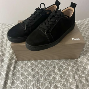 Christian Louboutin svarta sneakers - Snygga svarta sneakers från Christian Louboutin i mocka med klassisk röd sula och rund tå. Skorna har svarta snören och diskreta detaljer, perfekt för dig som gillar lyxiga och stilrena sneakers med exklusiv känsla.