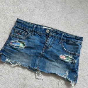 Blå jeanskjol från Hollister - Säljer en skor snygg kort jeanskjol från Hollister med slitna detaljer och fransig kant. Kjolen har klassisk femficksdesign, låg midja och råa kanter för en avslappnad look. Perfekta för sommaren! Tyvär för små för mig så kan inte ta några bilder på
