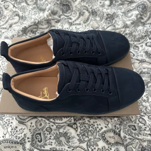 Christian Louboutin - Säljer ett par mörkblåa  Christian Louboutin med klassisk röd sula och diskret logga på insidan. Skorna har rund tå, snörning och är tillverkade i mocka med beige innersula. Perfekta för dig som gillar stilrena och exklusiva sneakers. Priset är inte hugget i sten och kom privat för fler frågor!