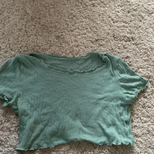Grön ribbad croppad t-shirt - Säljer en ljusgrön croppad t-shirt med ribbad struktur och korta ärmar. Toppen har vågig kant vid halsringning och nederkant för en extra detalj. Perfekt till sommaren!