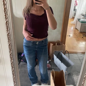 Blå bootcut jeans från H&M - Säljer ett par klassiska blå bootcut jeans från H&M med låg midja och justerbar midja. Jeansen har två knappar framtill och raka ben med lätt utsvängd form. Perfekta för dig som gillar en tidlös denimlook. Observera att inga bakfickor finns!💗