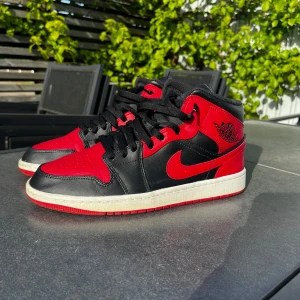 Nike Air Jordan 1 Mid Banned - Säljer ett par Nike Air Jordan 1 Mid i svart och rött med klassisk design. Köpta på merch sweden, skolåda finns kvar och ingår.