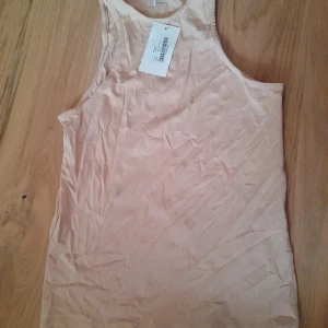 Beige linne topp från NLY Trend - Säljer en enkel och stilren beige linnetopp från NLY Trend. Toppen är ärmlös med rund halsringning och tillverkad i mjuk bomullsblandning. Perfekt för varma dagar eller som lager under andra plagg. Oanvänd. Reform top. Rose dust