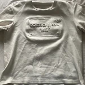 Vit t-shirt från Dolce & Gabbana - Snygg vit t-shirt från Dolce & Gabbana med upphöjd logotyp på bröstet. Klassisk rund halsringning och korta ärmar. Perfekt för dig som gillar stilrena och exklusiva plagg.