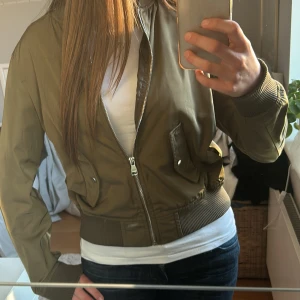 Grön bomberjacka från Bershka - Säljer en olivgrön bomberjacka från Bershka med dragkedja framtill och två fickor med knappar. Jackan har ribbade muddar vid ärmslut, midja och hals. Perfekt cool vårjacka till våren!💞💞💞
