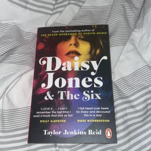 Daisy Jones & The Six - En populär roman på engelska, 'Daisy Jones & The Six', skriven av Taylor Jenkins Reid. Boken har ett färgstarkt omslag med ett porträtt och stora vita bokstäver. Perfekt för dig som gillar musik, 70-tal och dramatiska berättelser.