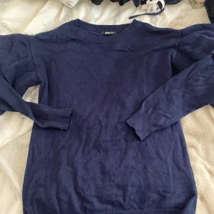 Mörkblå stickad tröja med volangärmar från Gina Tricot - Säljer en mörkblå stickad tröja från Gina Tricot i storlek XS. Tröjan har långa ärmar med snygga volangdetaljer och ribbade muddar.🩷