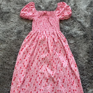 Rosa blommig klänning med puffärmar - Superfin rosa långklänning med blommigt mönster och puffärmar. Smockad överdel med rosett framtill och fyrkantig ringning. Perfekt för sommarens alla tillfällen! Helt ny aldrig använt innan!💕