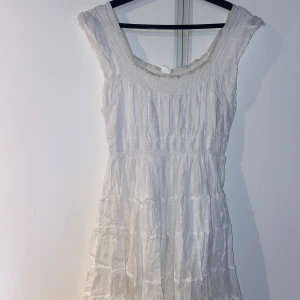 Vit medel-långklänning med volangdetaljer - Säljer en vit medel-långklänning med volangdetaljer och bred resår vid halsringningen.