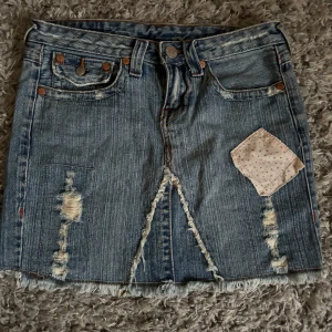Jeanskjol från True Religion - Säljer en lågmidjad jeanskjol från True Religion, slitna detaljer. Kjolen har klassiska jeansfickor och knappar med logga bak.🩷skriv vid frågor 🩷