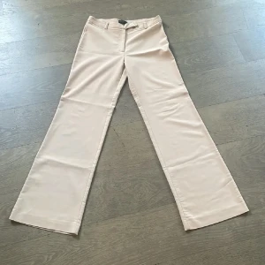 Beige lågmidjade kostymbyxor från Fransa - Stilrena beige kostymbyxor från Fransa med normal passform och raka, vida ben. Byxorna har hällor för bälte, diskret dragkedja och knapp framtill. Perfekta för en clean och klassisk look.