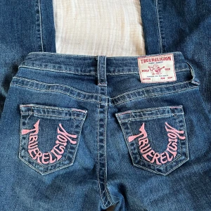 True Religion Bootcut Jeans - Säljer ett par blå lågmidjade True Religion jeans, modell Becca Mid Rise Bootcut. Jeansen har klassisk bootcut-passform, rosa broderad True Religion-logga på bakfickorna och tydliga sömmar. Skriv för fler funderingar eller bilder❤️