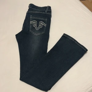 Mörkblå jeansbyxor med broderade bakfickor - Säljer ett par mörkblå jeansbyxor med snygga vita broderier på bakfickorna och kontrastsömmar. Bra normal passform och bootcut i benen. Säljer pga för små. Aldrig använda. Skriv för mer info/bilder