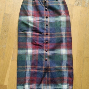 Lång rutig kjol  - En lång och snäv kjol av rutigt tyg. De fyra första knapparna är bara dekorativa men resten av knapparna är riktiga. Kjolen slutar precis över anklarna på mig som är 160 cm.